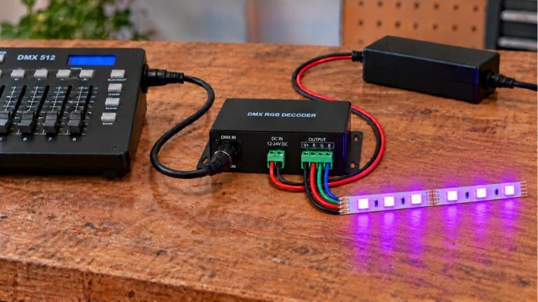 DMX controller and RGB decoder connected to a straight illuminated RGB LED strip sample on a workbench.