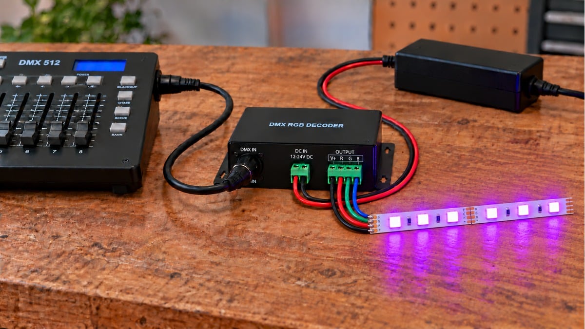 DMX controller and RGB decoder connected to a straight illuminated RGB LED strip sample on a workbench.