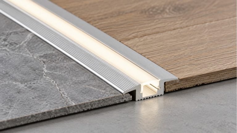 Illuminated aluminum transition profile joining stone tile and wood flooring.