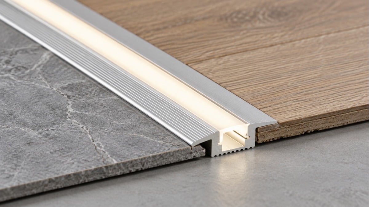 Illuminated aluminum transition profile joining stone tile and wood flooring.