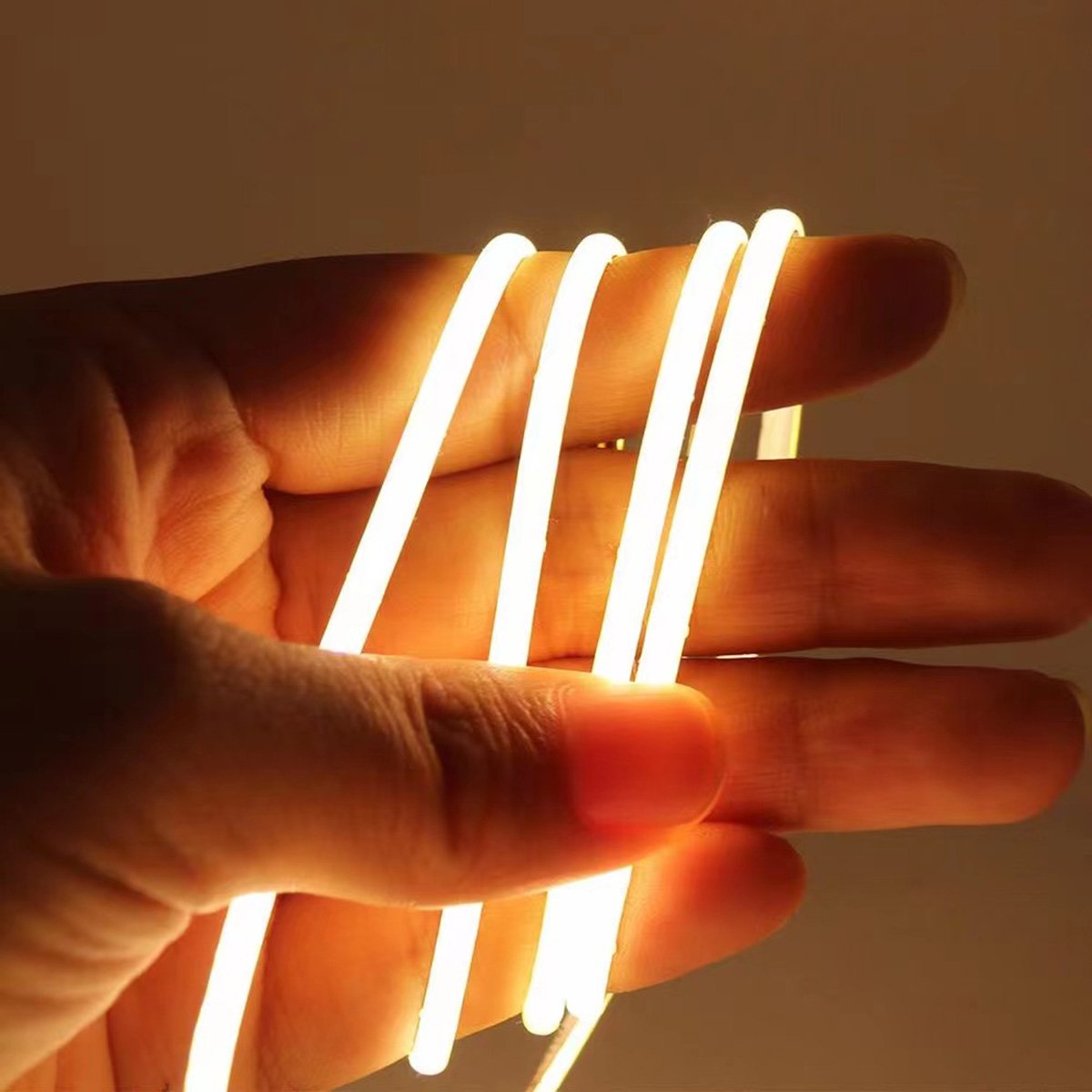 Warm white COB LED strip held in a hand showing a seamless light line