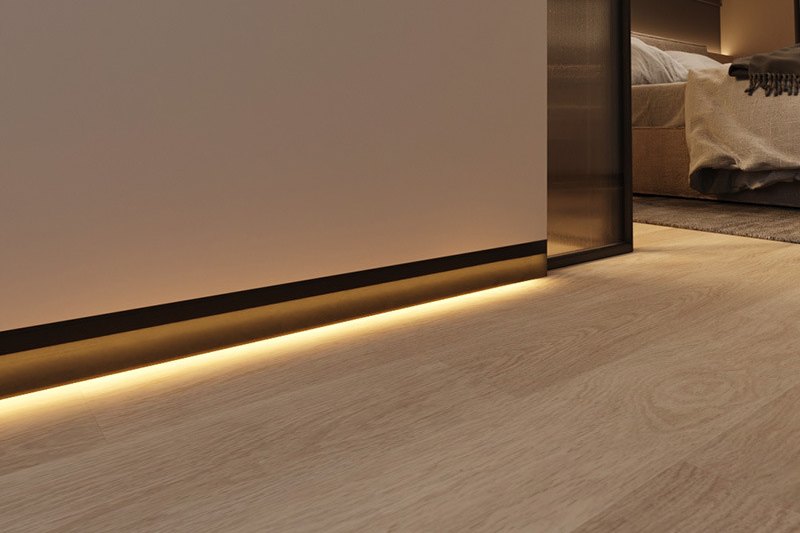 Warm LED strip in a black aluminium skirting profile lighting an oak floor at a bedroom doorway