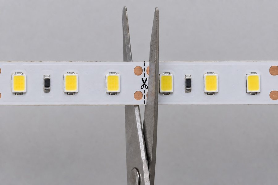 Scissors lined up on the marked cut line between the copper pads of an LED strip