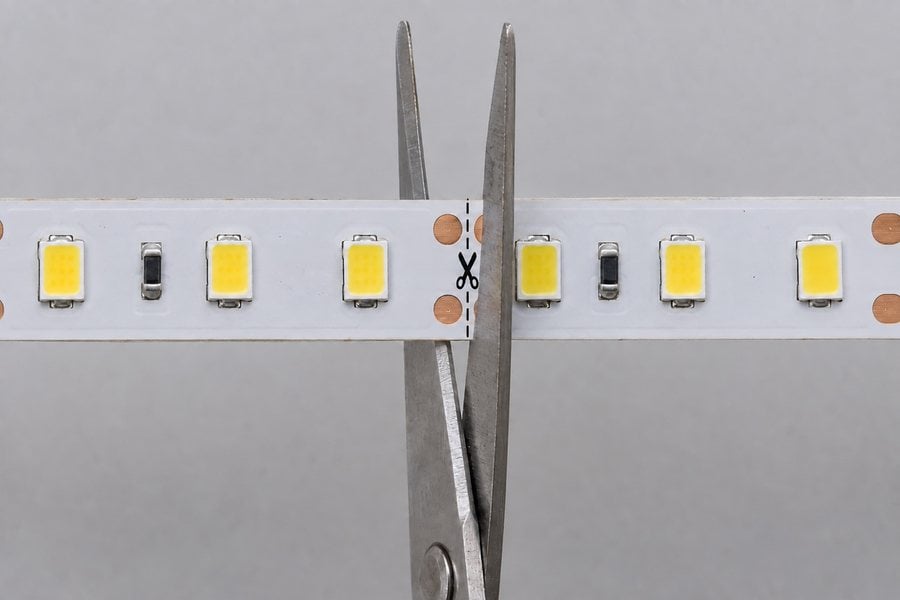 Scissors lined up on the marked cut line between the copper pads of an LED strip